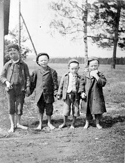 Äldre foto på fyra barn, hagmark och skog i bakgrund