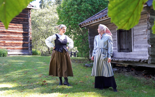 Två kvinnor med äldre kläder vid äldre hus